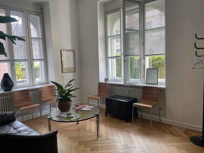 Wartezimmer mit Ledersofa, Glastisch und Altbaufenstern